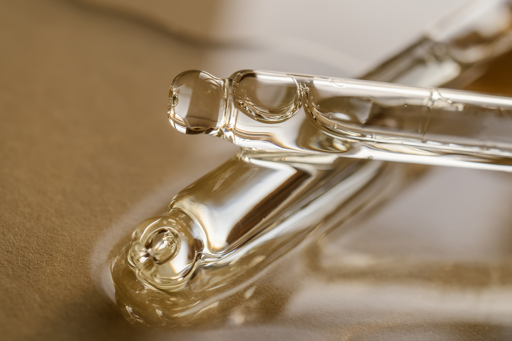 Pipettes with Oil or Serum on a Golden Background.